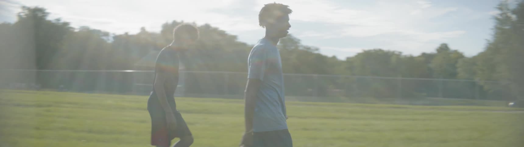 A teenage boy is carrying a football while walking on a field with another boy during the day