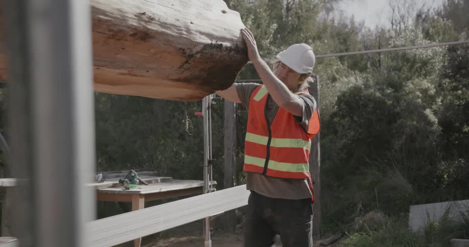 A construction worker guides a large piece of wood