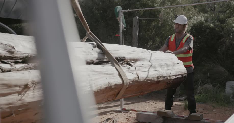 A man helps to guide timber being placed by a crane