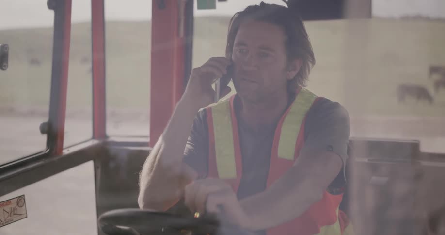 A man sits in the cab of construction equipment and talks on the phone