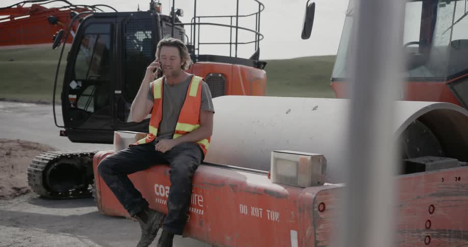 Man sitting on a steamroller while talking on the phone