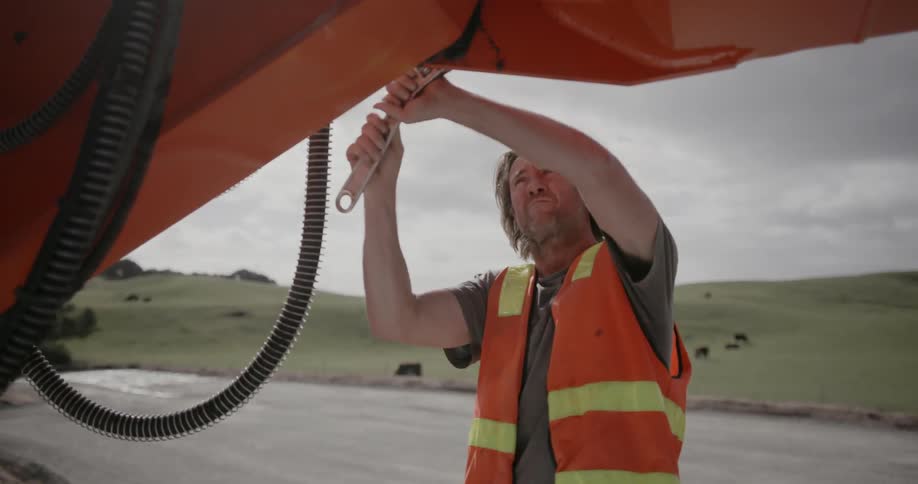 A man uses a large wrench on a piece of construction equipment