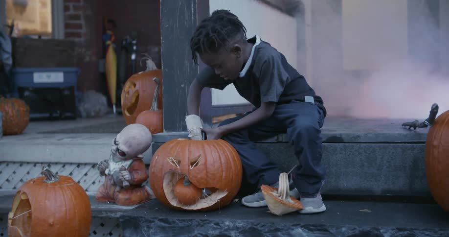 A young boy lights a candle inside a pumpkin