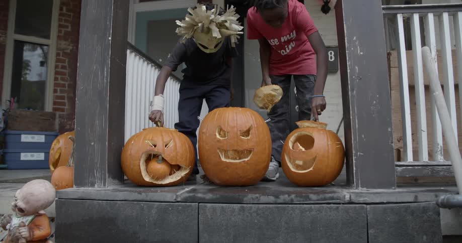 Two young kids lift tops off of carved pumpkins