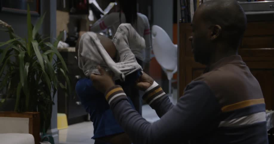 A man helps his son put on a shirt
