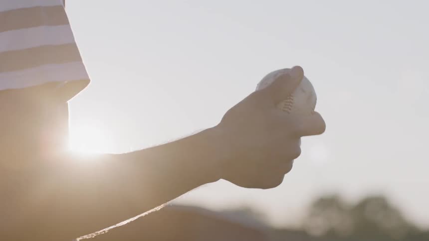 A man twirls a baseball between his fingers and prepares to pitch