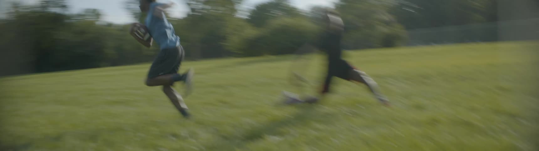 A boy carrying a football runs past his friend