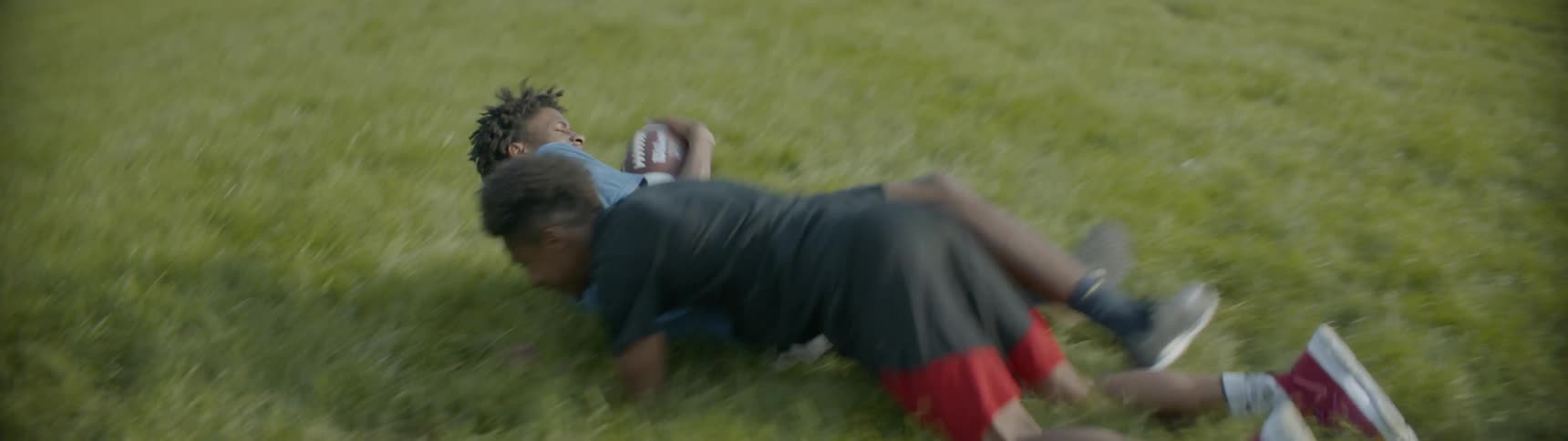 A boy tackles his friend as he tries to run by with the football