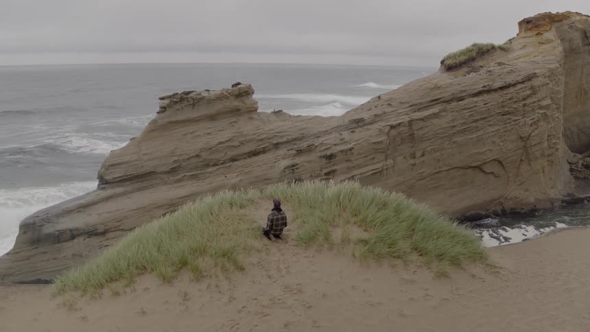 A man kneels at the sand cliff by the ocean