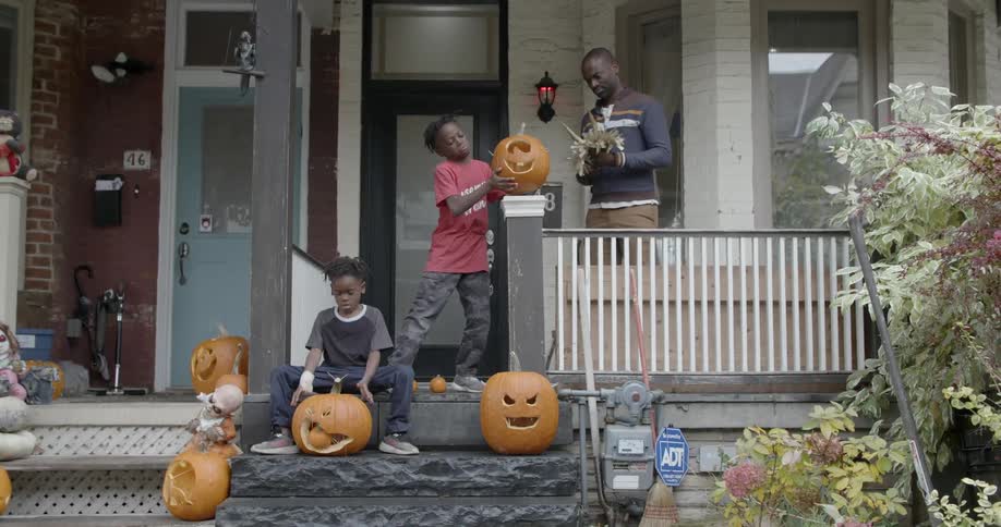 Children work on carving pumpkins in front of a home