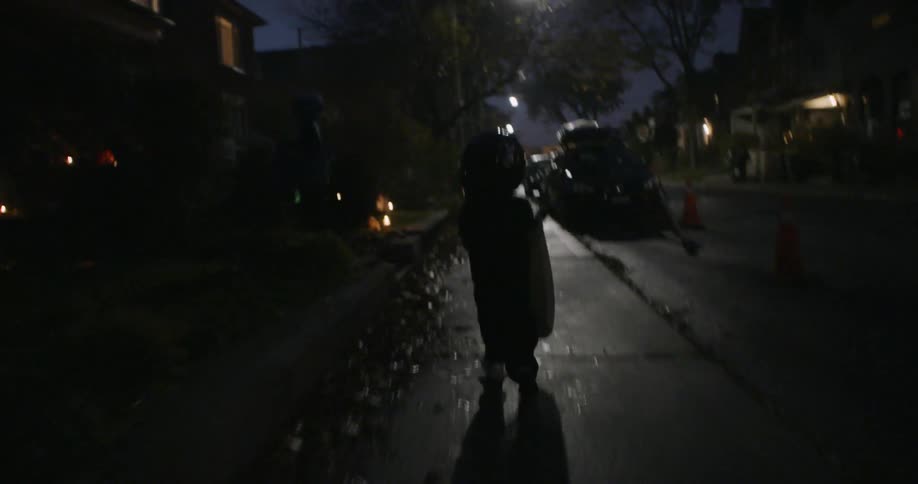 A trick or treater is running down the sidewalk