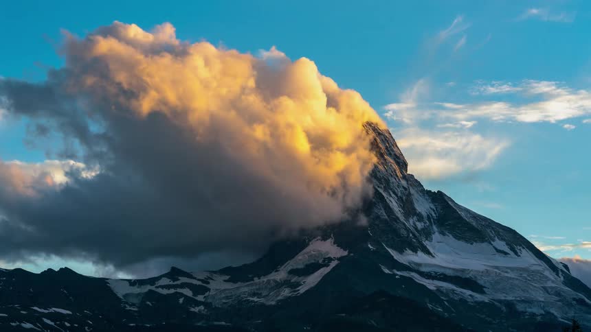 Clouds gather and pass above a tall frozen mountain top