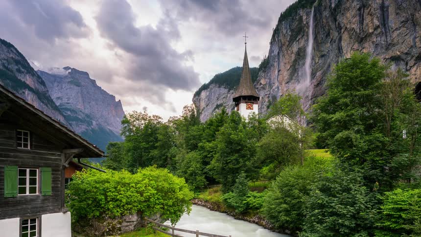 Water flows down a waterfall near a church surrounded by mountains