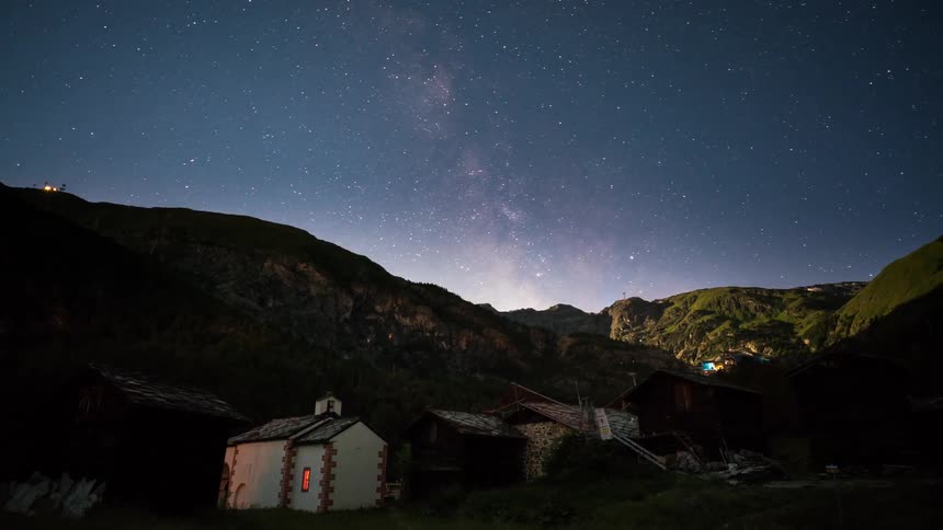 The stars move over a church and a mountain range at dawn