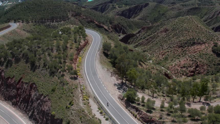 A bicyclist rides down a mountain road in impressive green scenery in the Sierra Nevada mountain range