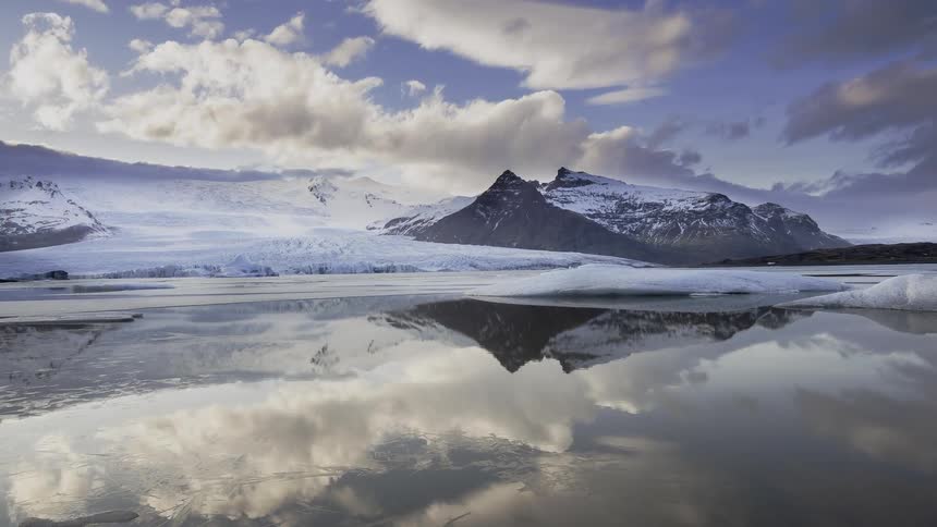 Clouds pass above the snowy mountain and lake