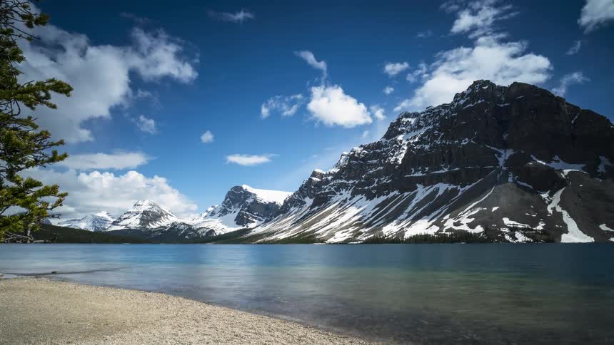 Scenic clouds pass over the Canadian Rockies and a lake on a sunny day in Banff