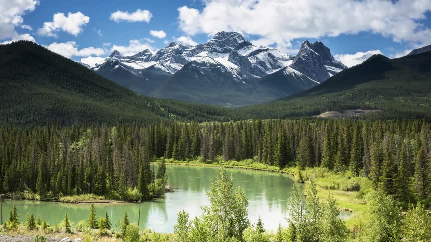 Clouds pass above a green valley and lake at the foot of the Canadian Rockies at Exshaw, Banff