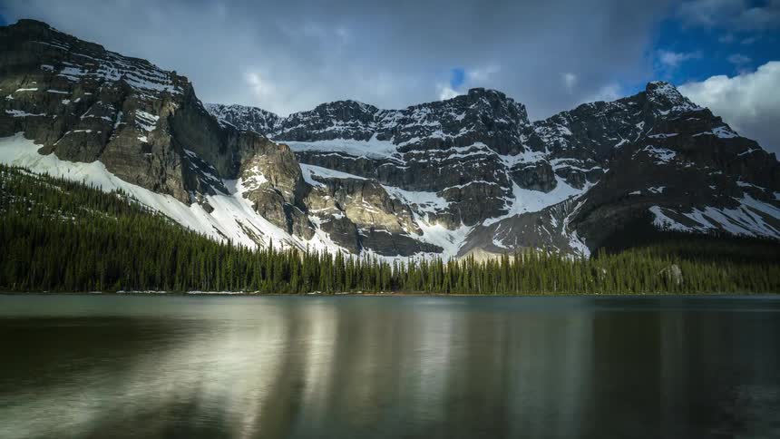 The clouds move fast over the mountains, forest and lake in Banff
