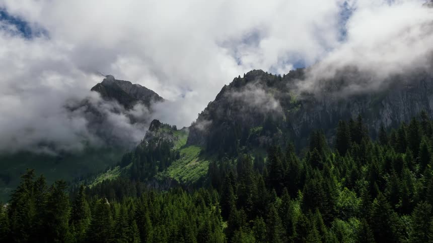 The tree covered mountains are covered with clouds ahead