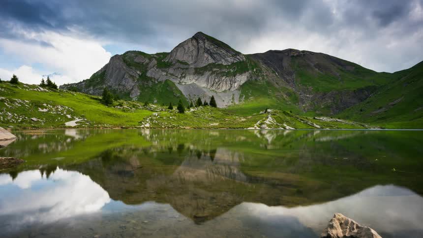 Drifting clouds and a mountain are reflecting in a lake during the day