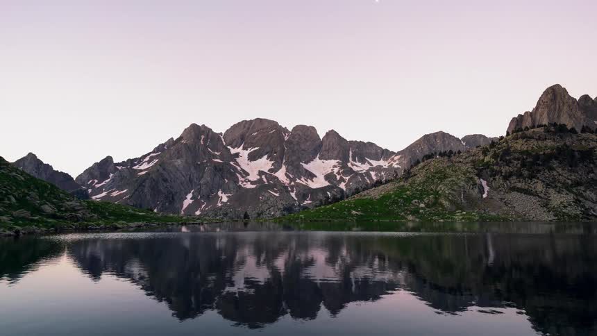 The sun rises across the sky above a secluded mountain and lake in the Catalan Pyrenees