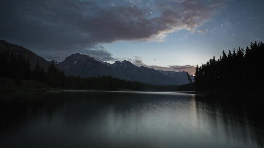 Clouds pass above the Johnson lake and mountains as the sun rises in Banff National Park