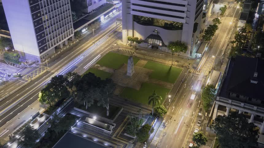Traffic is flowing on city streets near a park throughout the night