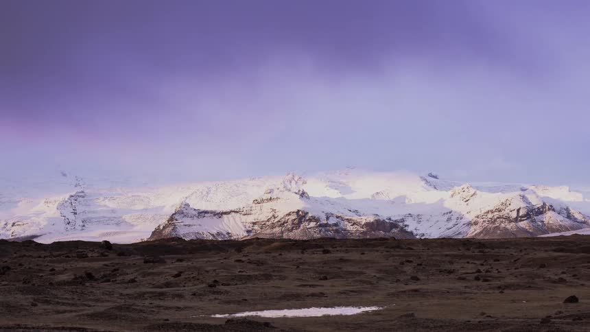 Clouds are drifting over a glacier and snow covered peaks at dawn