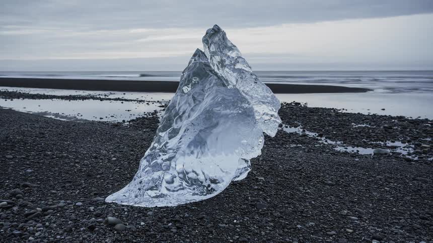 A large piece of ice sits on the beach shore