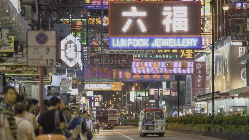 Crowd of people standing on the edge of a busy city street at night