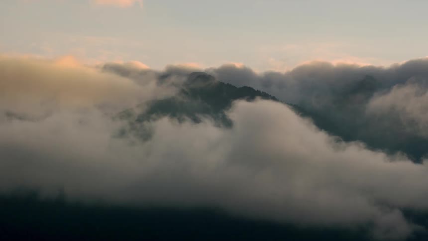 Clouds billowing and flowing over a mountain top covered in trees