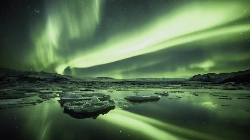 Northern lights flash above the ice covered field and water