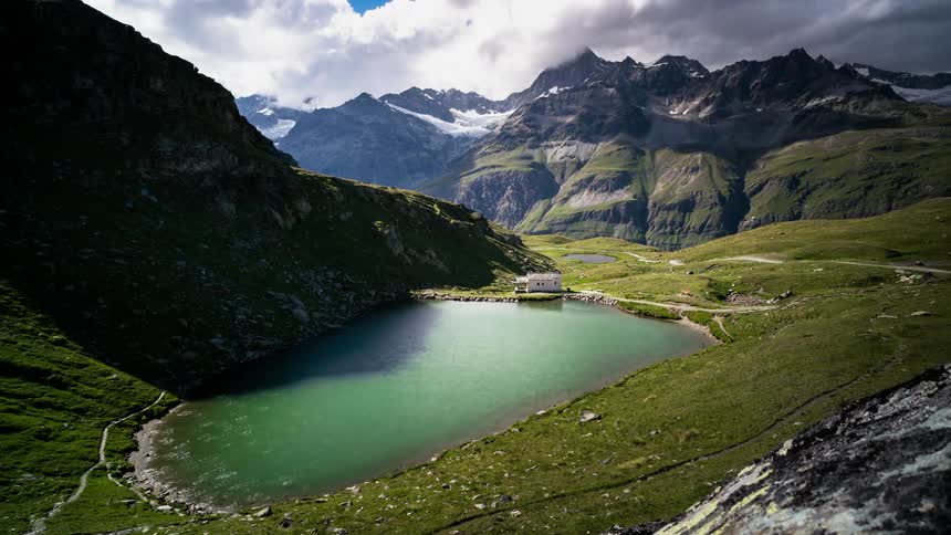 Clouds pass above the mountains and a clear green lake
