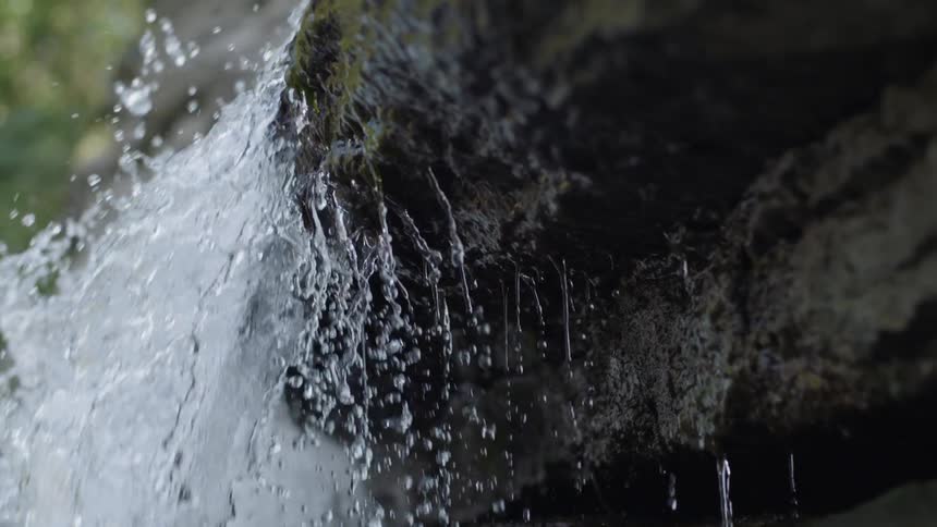 Water flowing over a rock in a stream is splashing and dripping
