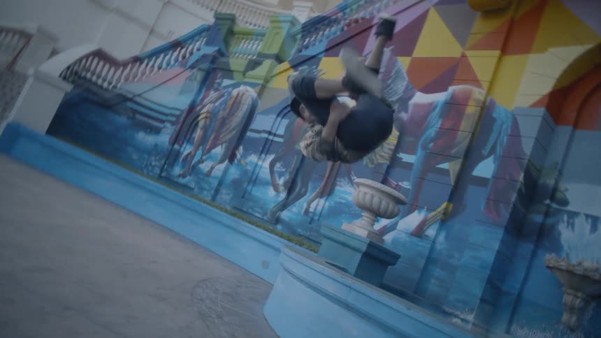 A man does a flip off a step in front of a building with a mural