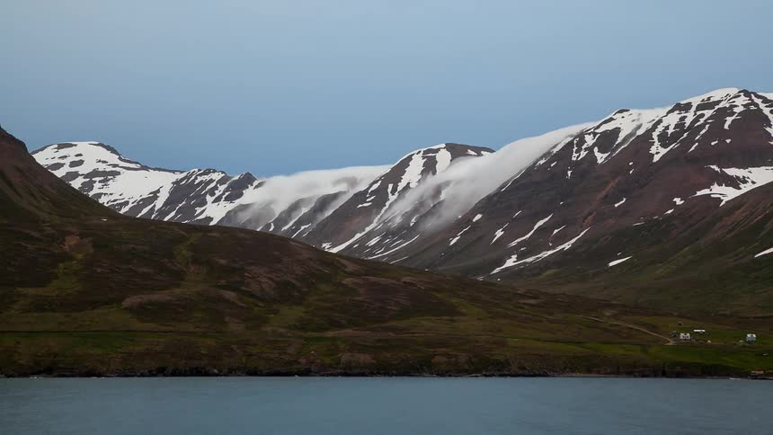 Wind is blowing drifts of snow across a mountain ridge during the day