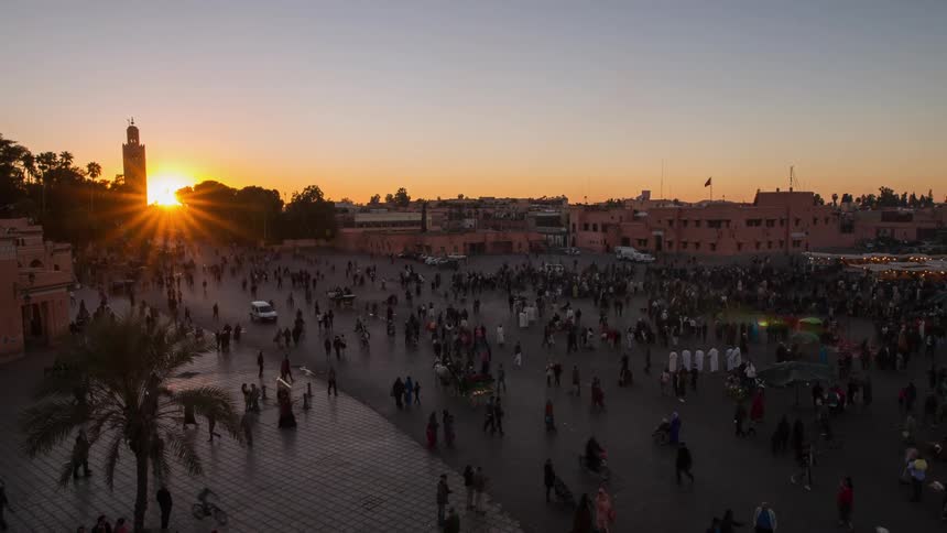 People walk and drive along this large road in the oriental city at sunset