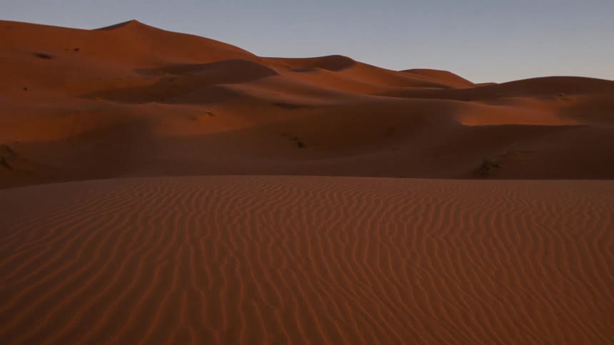Sand drifts lightly across the Sahara desert as the sun sets