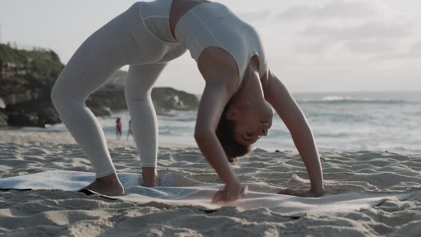 A woman does yoga on a beach at sunset