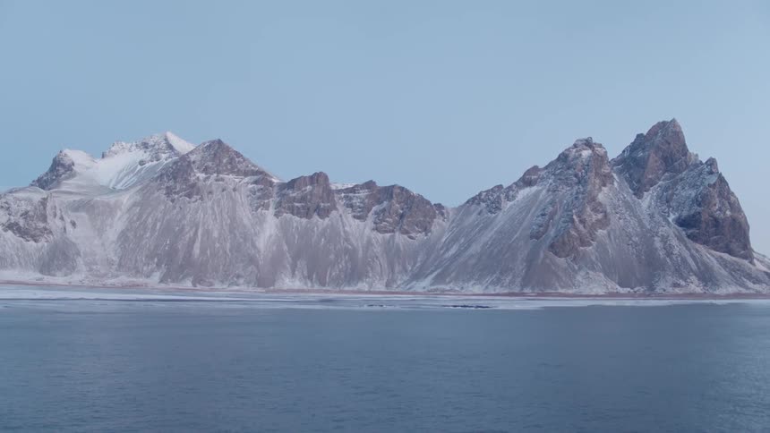 Tall mountains tower over the partially frozen waters