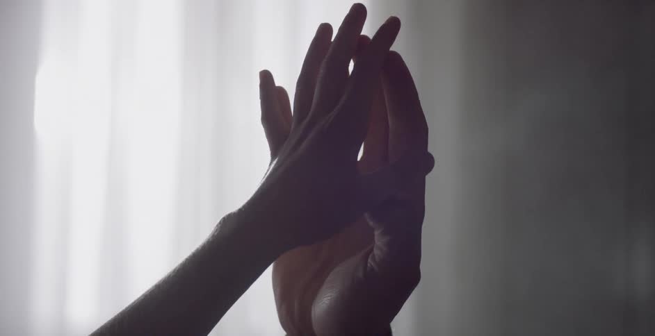 Two hands touch in the sunlight in front of a window