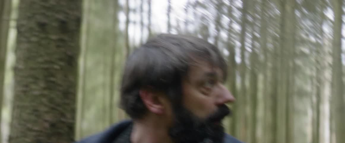 A man with a beard is in the woods and looks scared