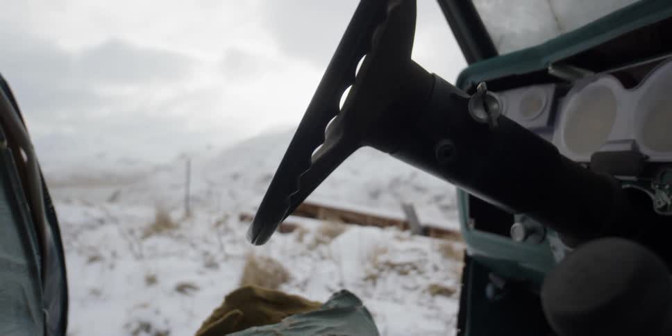 An abandoned car missing a door sits in a snowy field
