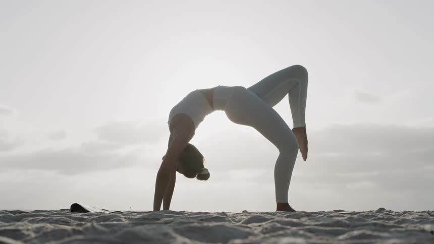 Woman practices yoga on the beach on a sunny day