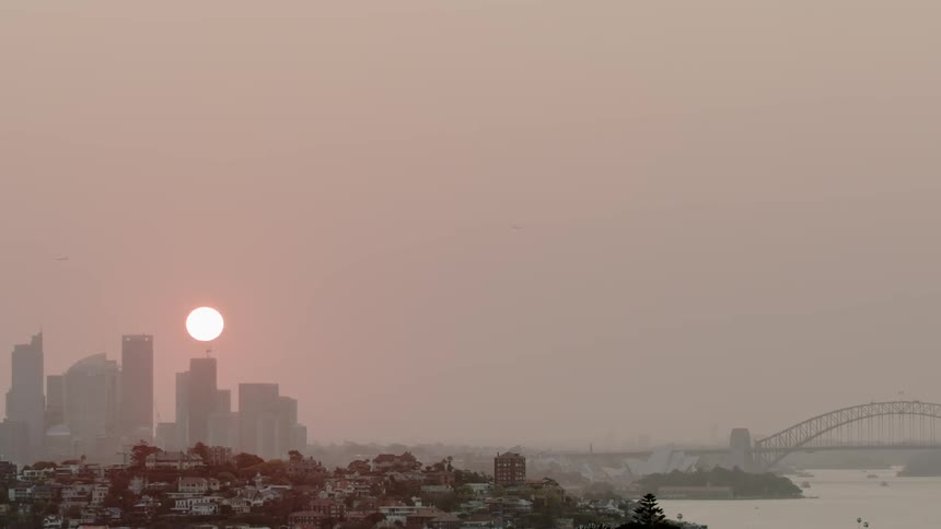 The sun begins to set behind tall city buildings