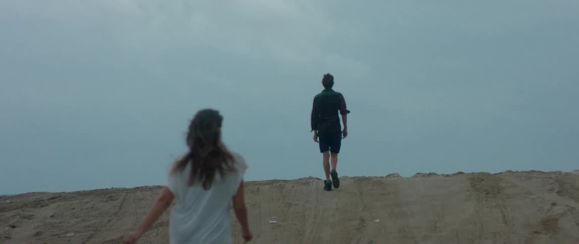 A woman is following a man as they walk up a dirt road on a cloudy day