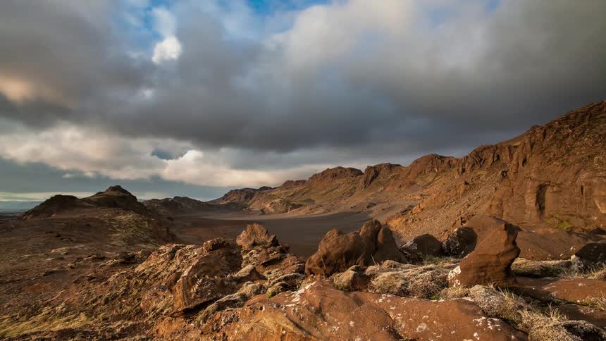 Clouds pass above the clay colored dirt by small mountains