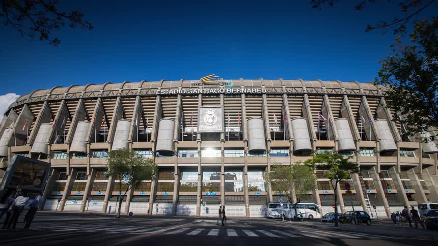 People mill about and walk past Santiago Bernabeu stadium on a sunny day