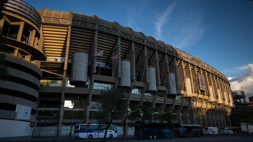 People travel along the Santiago Bernabeu stadium outside as the sun sets